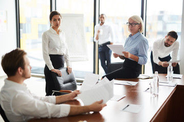 Female economists looking at one of colleagues while discussing financial papers at meeting