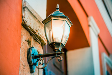 Lit vintage lantern hanged on an orange building at evening
