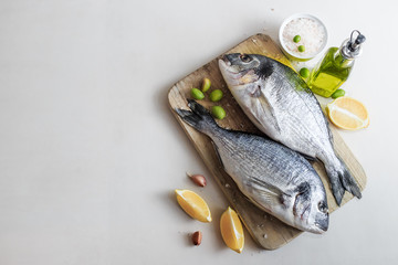 Fresh raw dorado or sea bream fish on a wooden kitchen board with lemon slices, spices, Himalaya pink salt, olive oil. Light background. Mediterranean Kitchen. Place for text