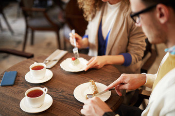 Guy taking piece of dessert from plate while having tea time in cafeteria with girlfriend