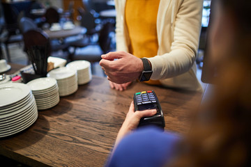 Client with smartwatch keeping his wrist over payment machine while paying for order in cafe