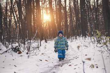 Small child walking on a snowy path among gloomy forest.
