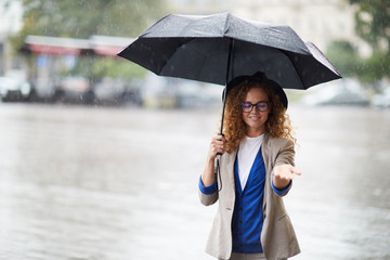 Young woman under umbrella stretching out her hand to catch raindrops