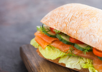 Fresh healthy salmon sandwich with lettuce and cucumber on vintage chopping board on black stone background. Breakfast snack. Diet food