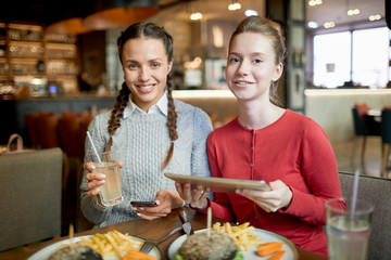 Two happy teenage girls in casualwear sitting by served table in cafe and having good time