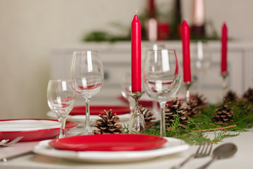 Merry Christmas and Happy New Year! Тable setting festive decor - white and red dishes, red candles in the candlesticks, juniper branches and fir cones.