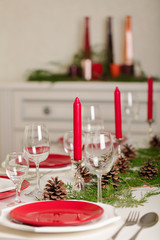 Merry Christmas and Happy New Year! Тable setting festive decor - white and red dishes, red candles in the candlesticks, juniper branches and fir cones.