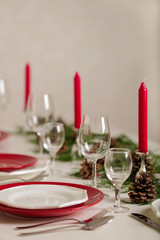 Merry Christmas and Happy New Year! Тable setting festive decor - white and red dishes, red candles in the candlesticks, juniper branches and fir cones.