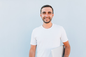 Portrait of a smiling young man standing with laptop against blue background