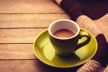 Green cup of the coffee and vintage scarf on wooden background. Photo with filter as a retro color image style.