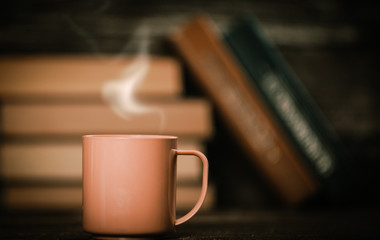 Books in bokeh and cup of coffee on wooden background.