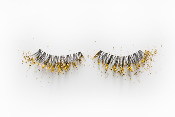False eyelashes with gold sparkles on a white background.
