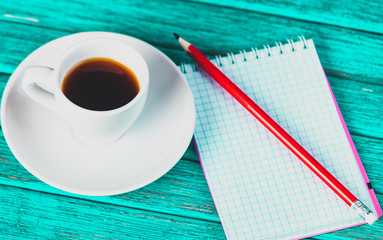 Cup of coffee and notebook with pen on blue color table