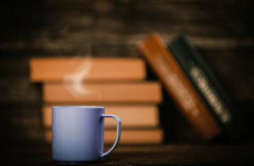 Books in bokeh and cup of coffee on wooden background.