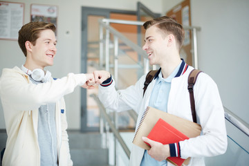 Two happy and successful students in casualwear bumping thair fists together