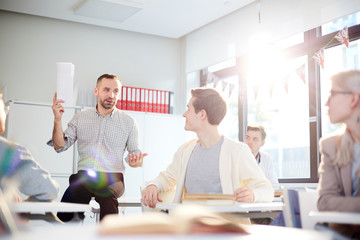 Successful teacher with papers looking at one of students while voicing his opinion about the essay