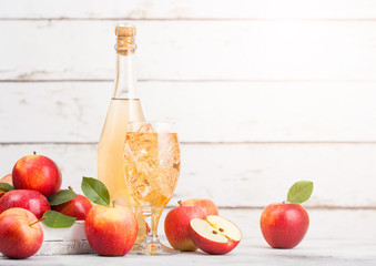 Bottle and glass of homemade organic apple cider with fresh apples in box on wooden background with sun light