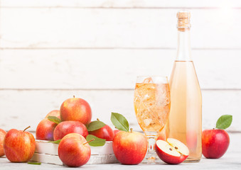 Bottle and glass of homemade organic apple cider with fresh apples in box on wooden background with sun light
