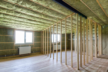 Construction and renovation of big light spacious empty room with oak floor, walls and ceiling insulated with rock wool, heating radiators under low attic windows and wooden frame for future walls.