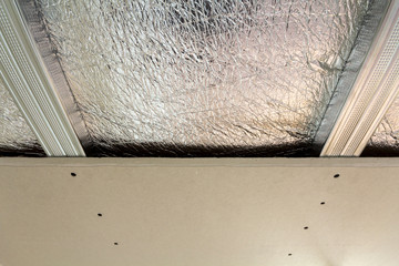Room under construction with silver aluminum insulation foil and drywall on walls and ceiling.