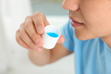 Man holding cap with mouthwash, closeup view. Teeth care