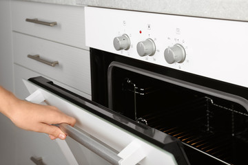 Woman opening empty electric oven in kitchen, closeup