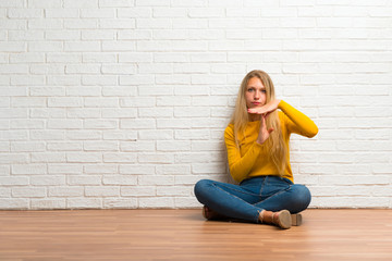 Young girl sitting on the floor making stop gesture with her hand to stop an act