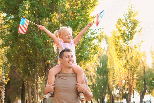 Man holding his daughter with American flags in park on sunny day