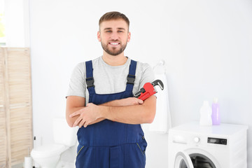 Young plumber with wrench near washing machine in bathroom