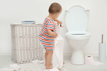 Cute toddler playing with toilet paper in bathroom