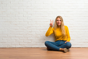 Young girl sitting on the floor happy and counting two with fingers