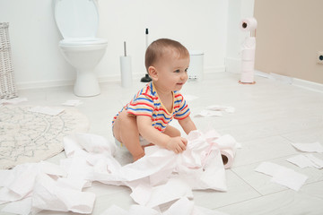 Cute toddler playing with toilet paper in bathroom