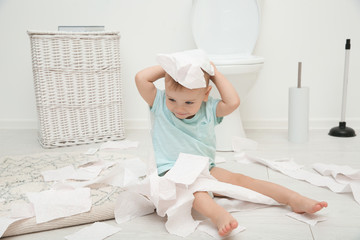 Cute toddler playing with toilet paper in bathroom
