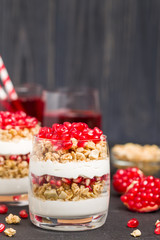 Pomegranate parfait - sweet organic layered dessert with granola flakes, yogurt and fruit seeds on black background.