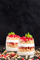 Pomegranate parfait - sweet organic layered dessert with granola flakes, yogurt and fruit seeds on black background.