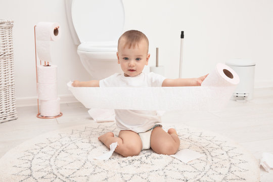 Cute toddler playing with toilet paper in bathroom