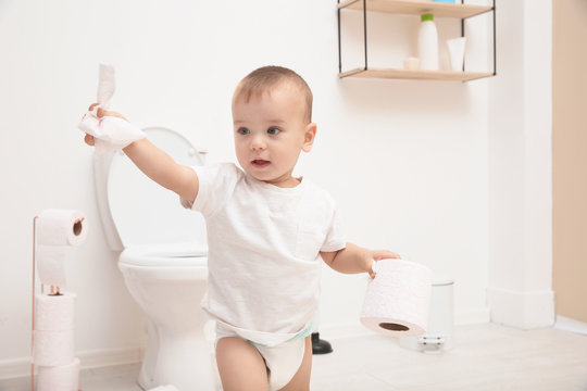 Cute toddler playing with toilet paper in bathroom