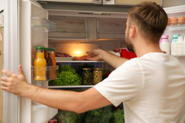 Young man taking sausages from refrigerator in kitchen