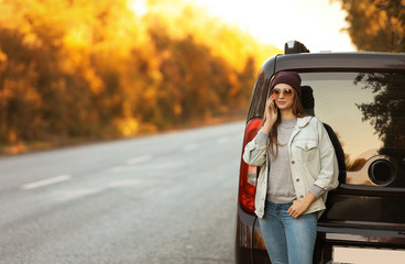 Young woman with mobile phone near car on country road. Space for text