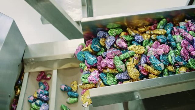 Candy factory. Bunch of wrapped candies falling from conveyor on packing containers in confectionery factory.
