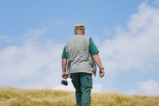 Traveler man photographed from the back in sports wear stands on the top of mountain. Blue sky with white clouds in a background.