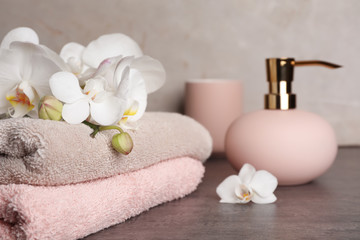 Stylish soap dispenser and towels with flowers on table