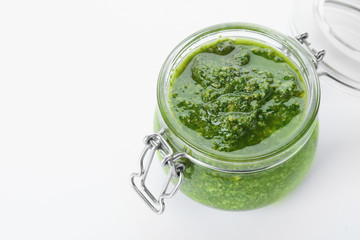 Homemade basil pesto sauce in glass jar on white background