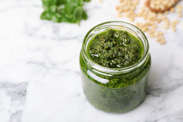 Homemade basil pesto sauce in glass jar on table