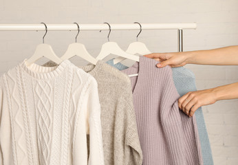 Woman choosing sweater on rack against brick wall