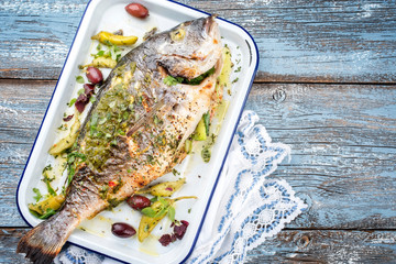 Fresh Greek barbecue gilthead seabream with peperoni and Kalamata olives as top view in a white...