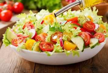 Cooking salad. olive oil pouring into bowl of fresh salad