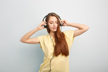 Long haired girl with headphones on her head  dressed in a yellow t-shirt and jeans stands on a...
