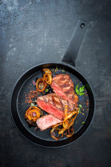 Modern Style classic dry aged sliced roast beef with fried onion rings served as top view in a minimalistic design cast-iron skillet