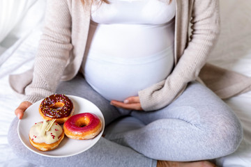 Schwangerschaft und ungesundes Essen: schwangere Frau hält einen Teller mit bunten Donuts